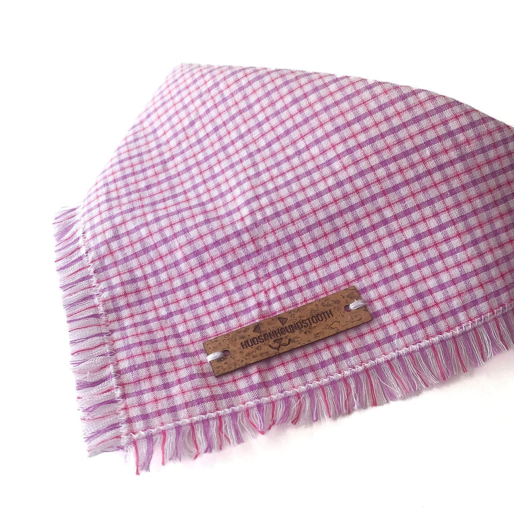 Image shows close up of Hudson Houndstooth Berry Sorbet Seersucker plaid dog bandana tied with delicate hand frayed edge and vegan cork leather label. Plaid features bright pink and purple colors perfect for summer.